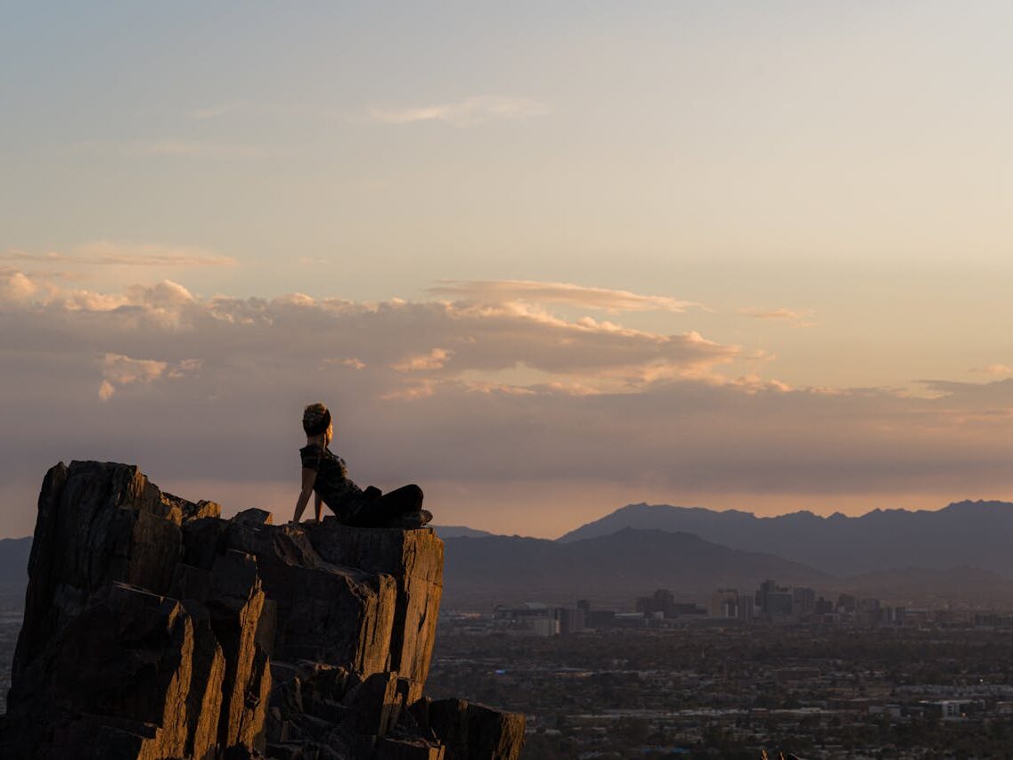a woman sitting on a mountain peak at sunset